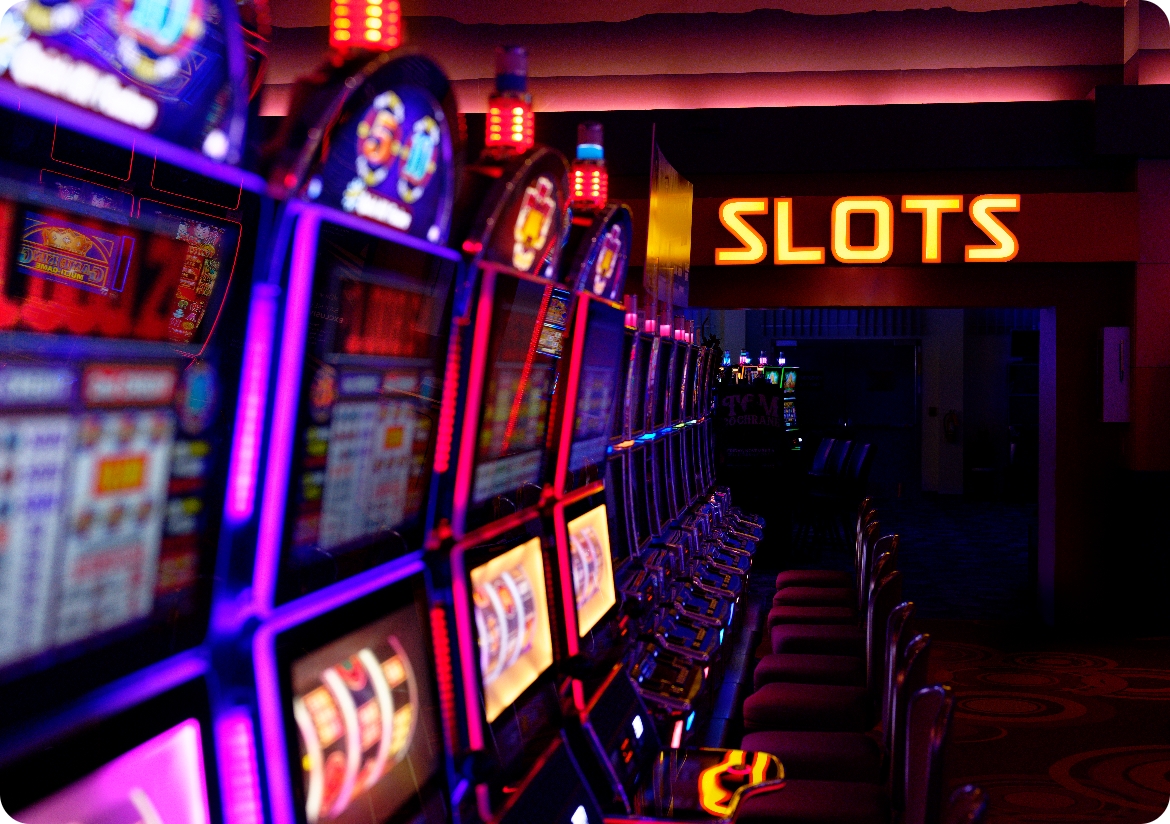 A row of slot machines with a Slots neon sign at the end.